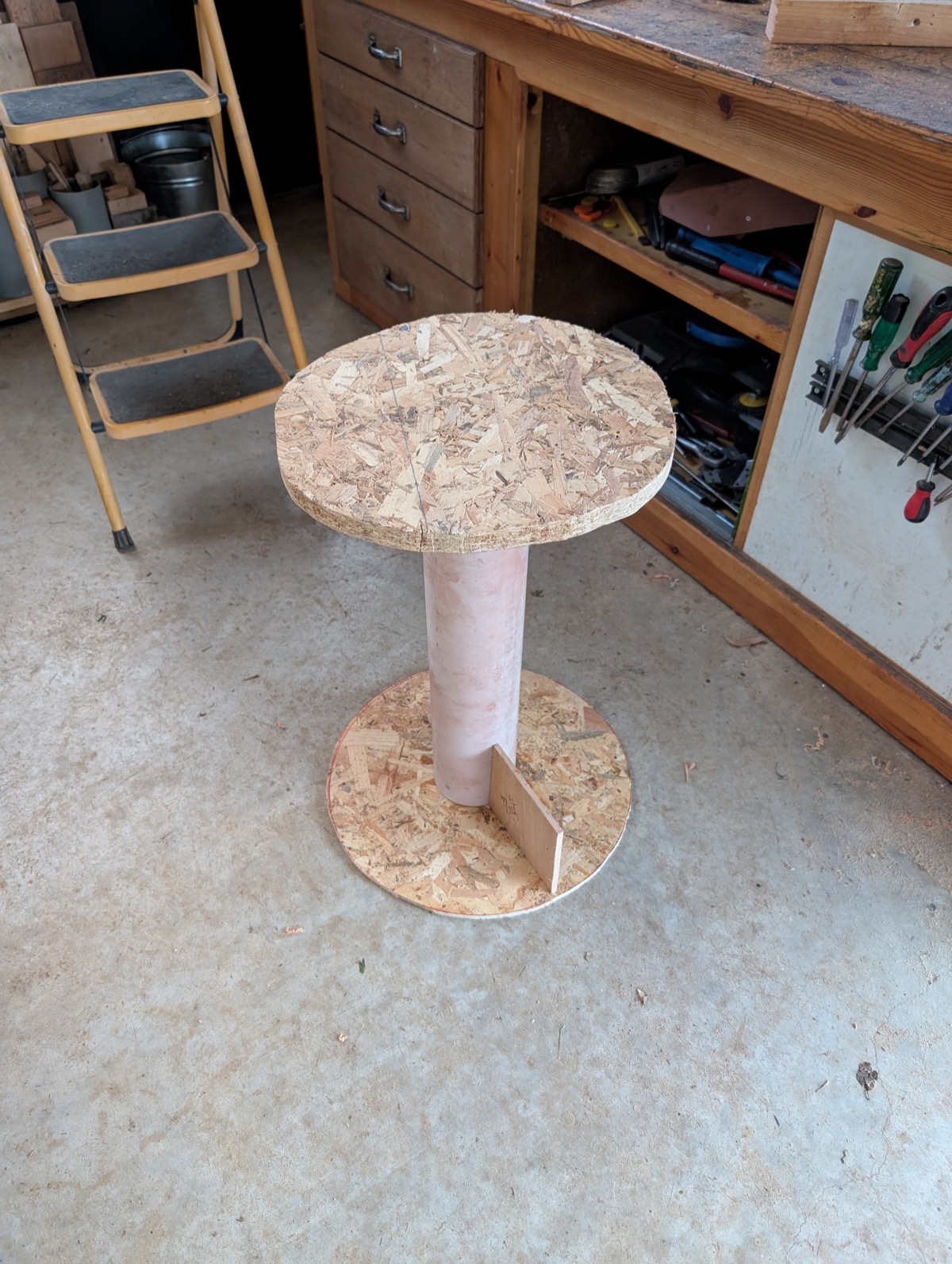 A mockup stool built from OSB board and a plastic pipe, testing proportions
