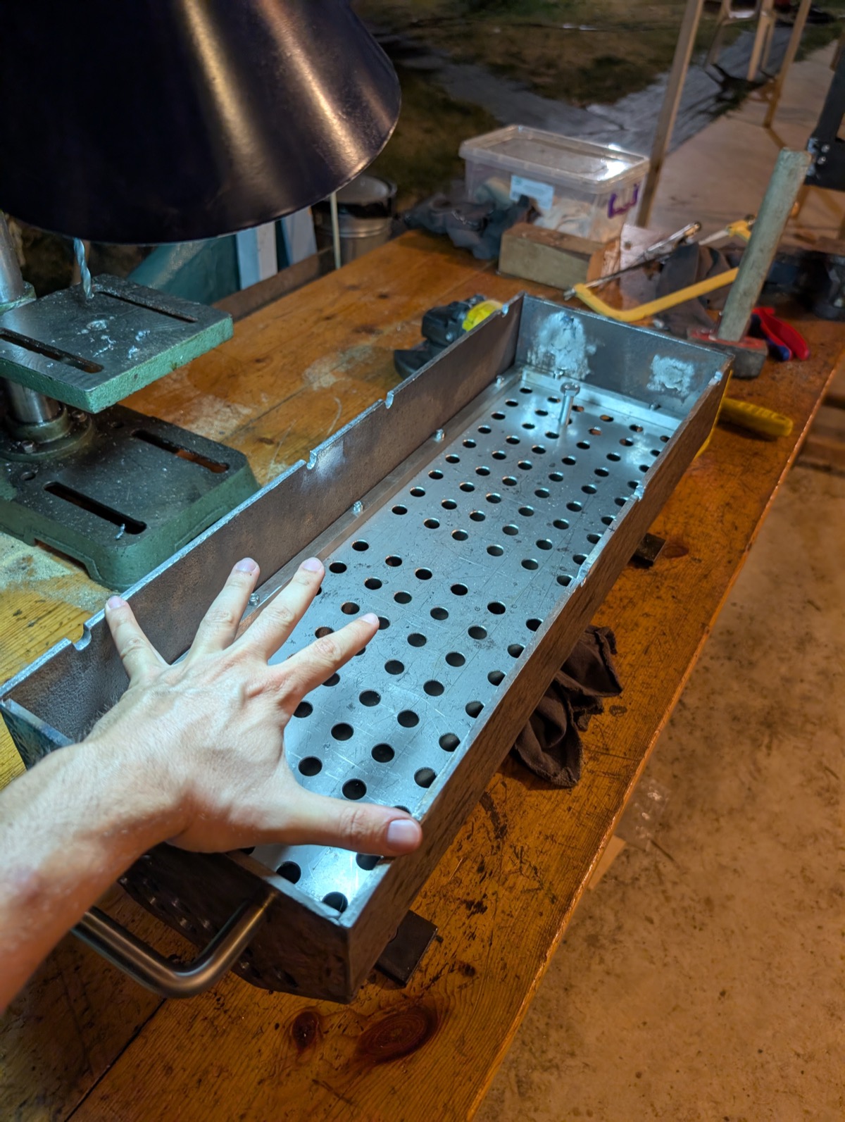 A hand resting on the perforated charcoal basket for scale