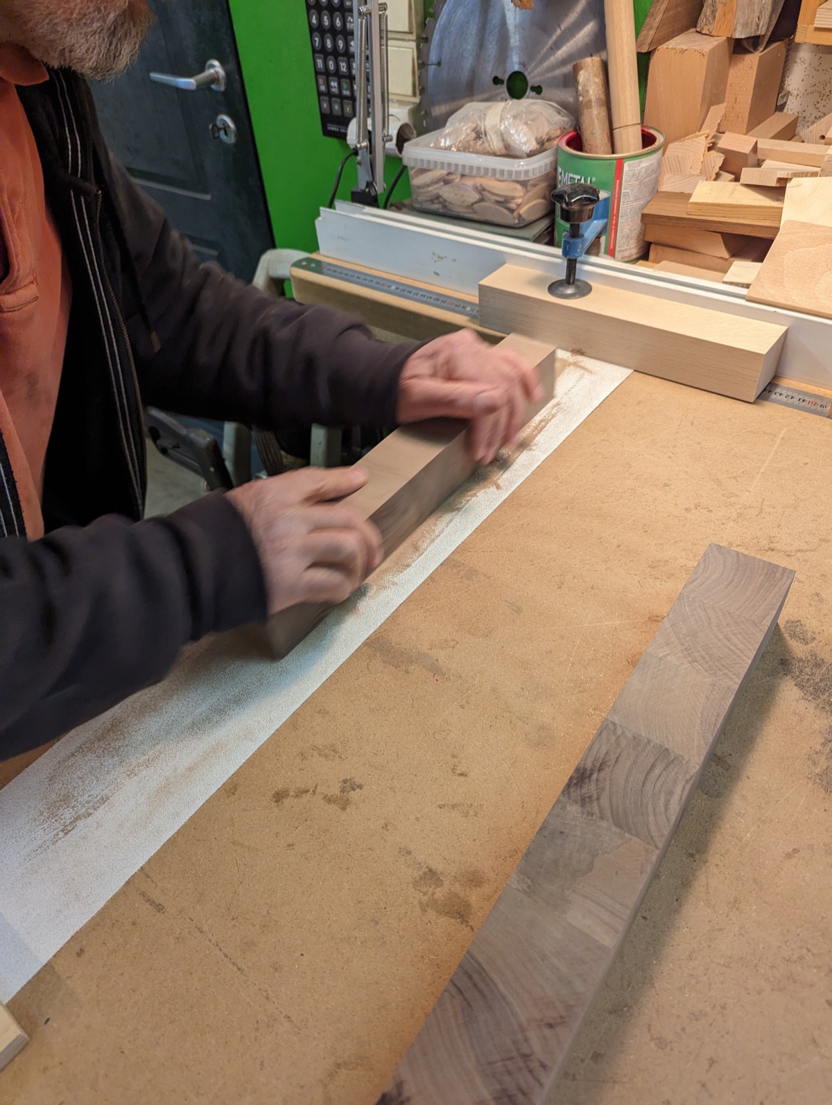 Hands sanding a single strip against paper on the bench