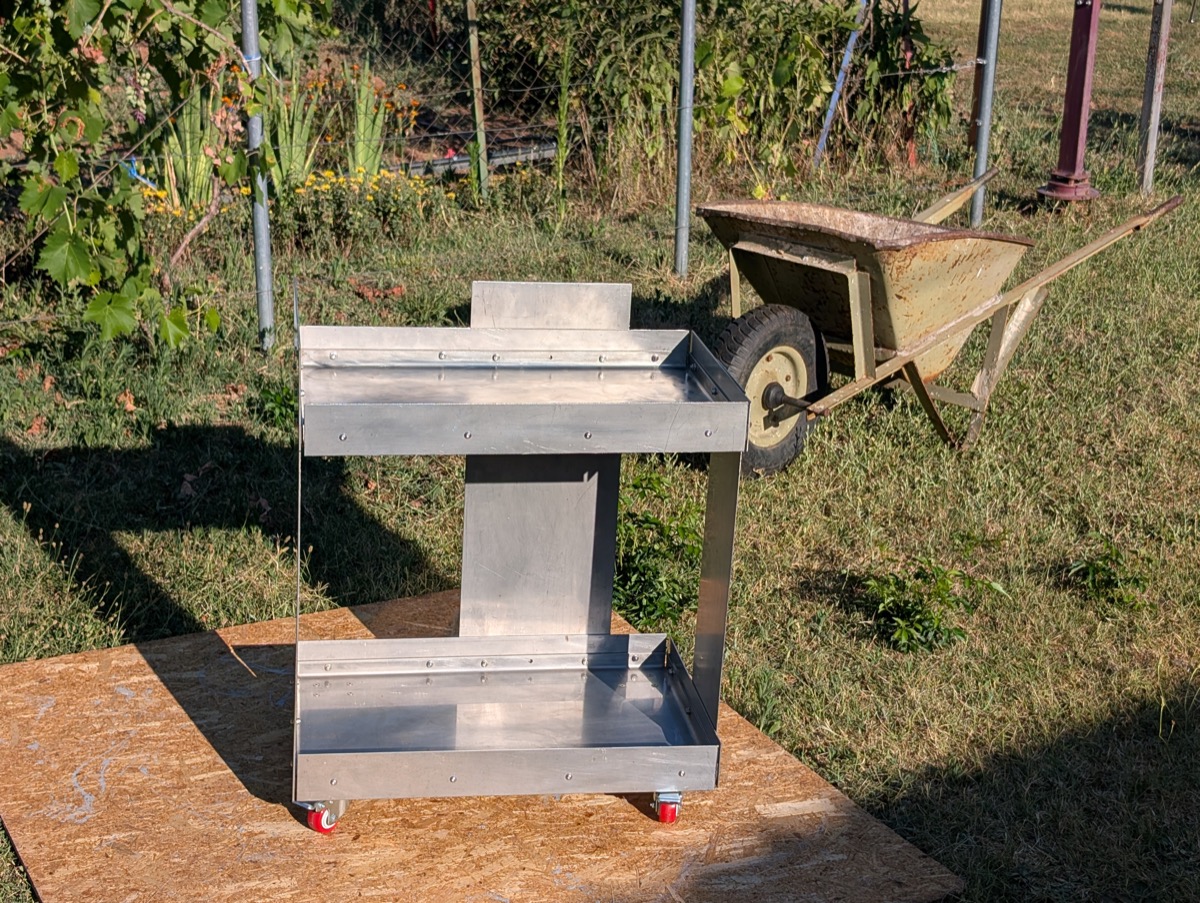 The finished stainless trolley in the garden, an old wheelbarrow behind it
