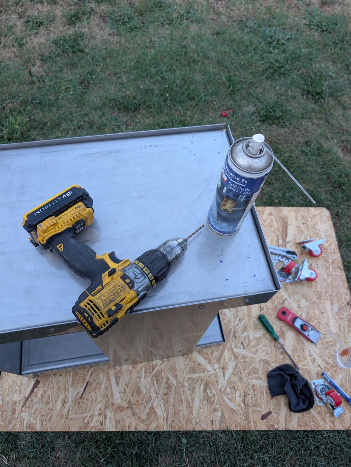 A drill, spray oil and casters laid out on the trolley's top shelf