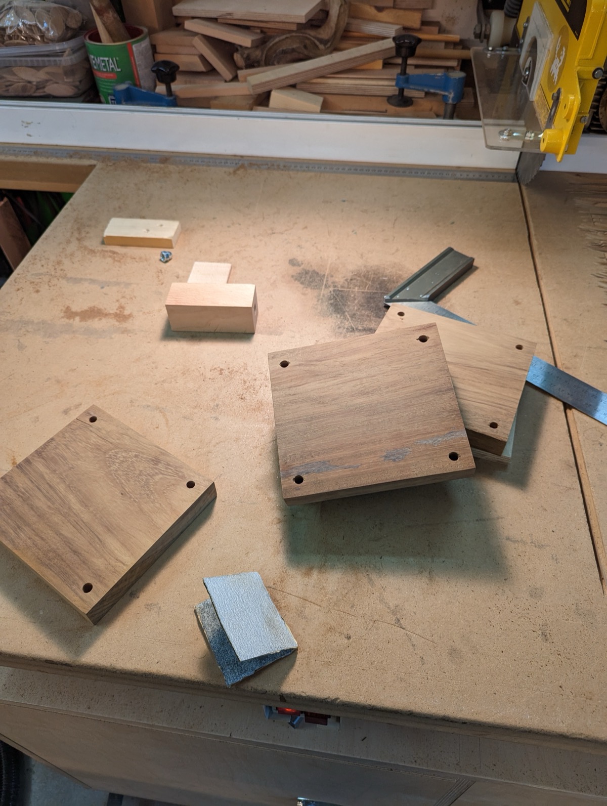 Four walnut shelves cut to size with a hole drilled at each corner, laid out on the bench