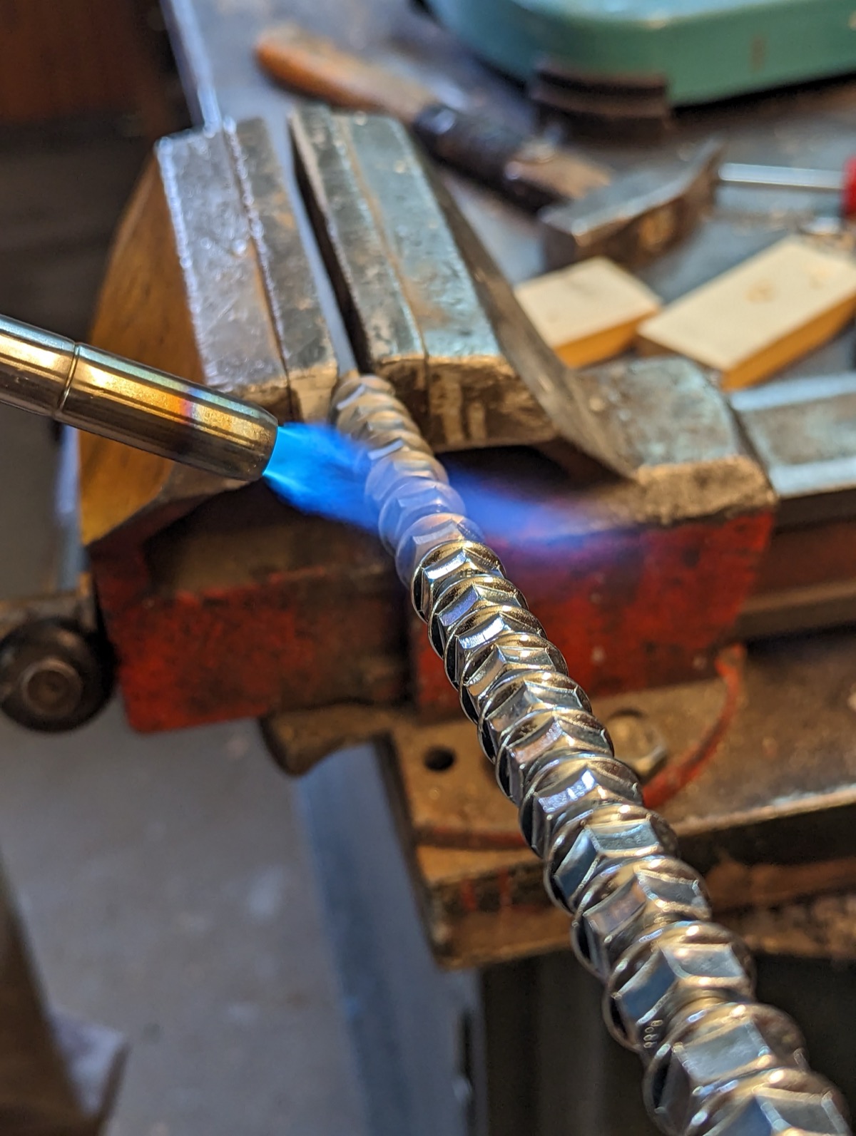A row of nuts threaded onto a rod held in a vice, heated with a blowtorch