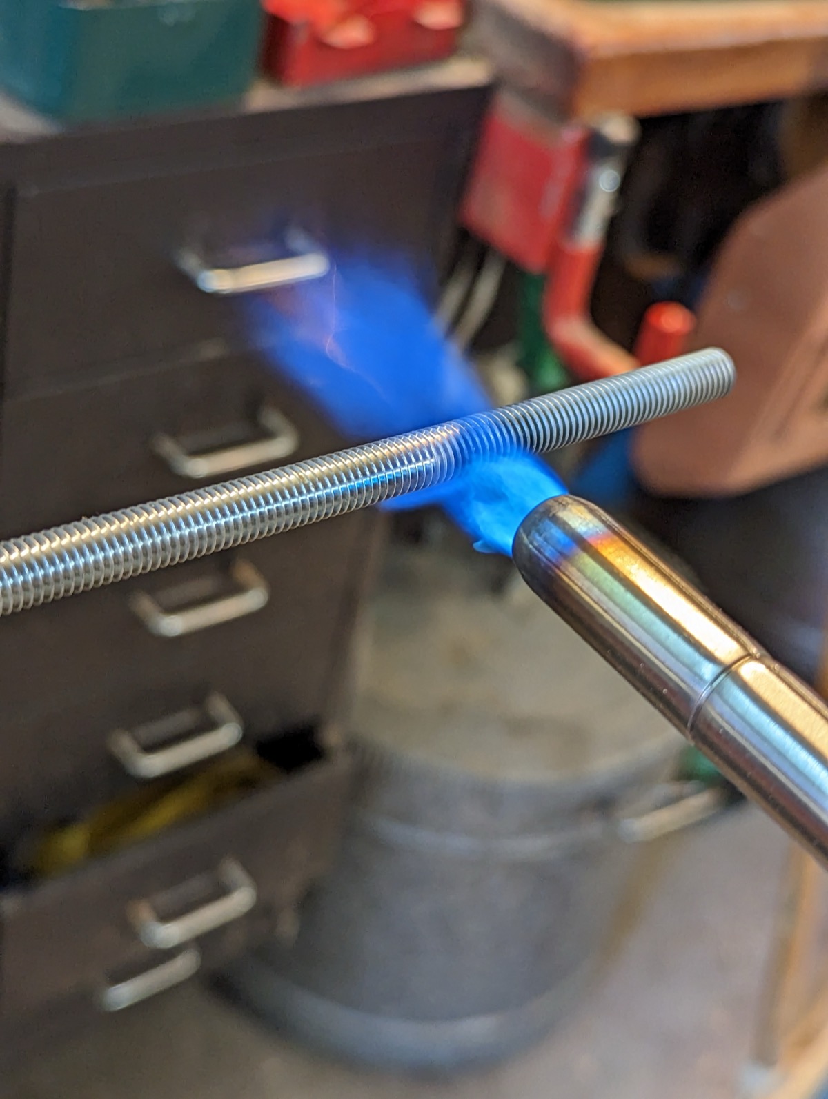 A blowtorch flame burning the zinc coating off a length of threaded rod