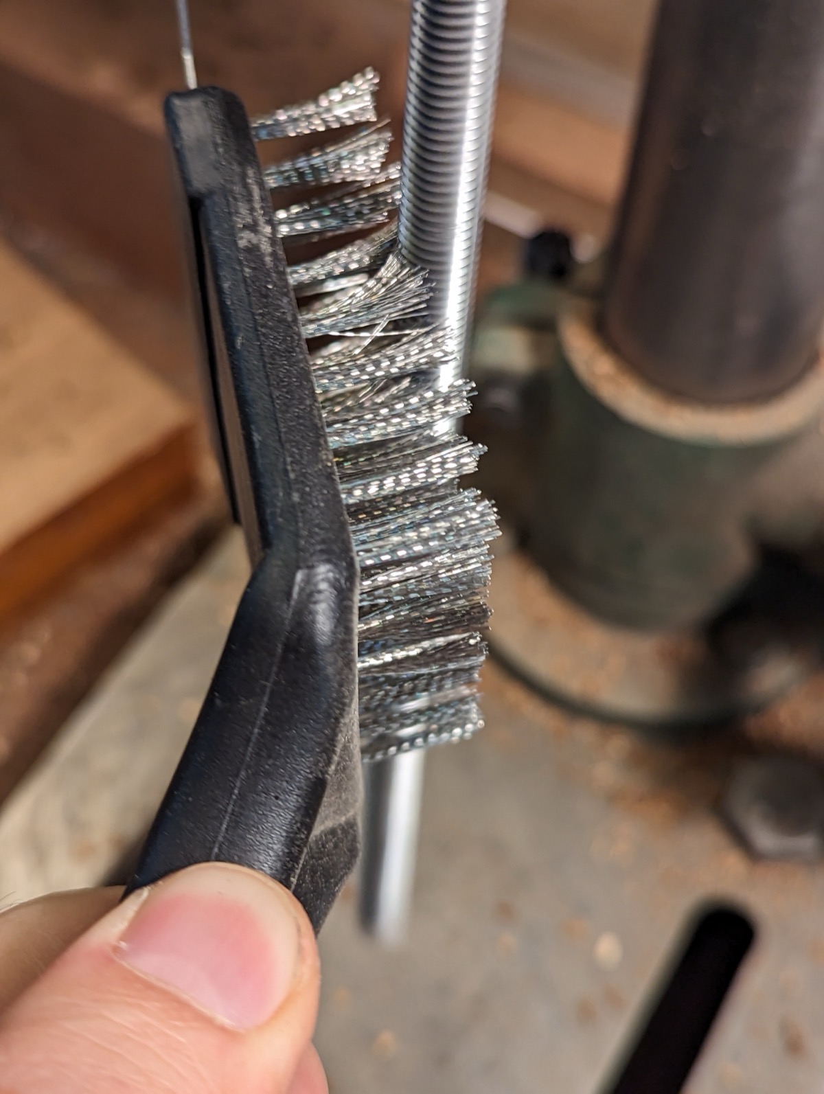 A wire brush scrubbing the burnt coating off the threaded rod