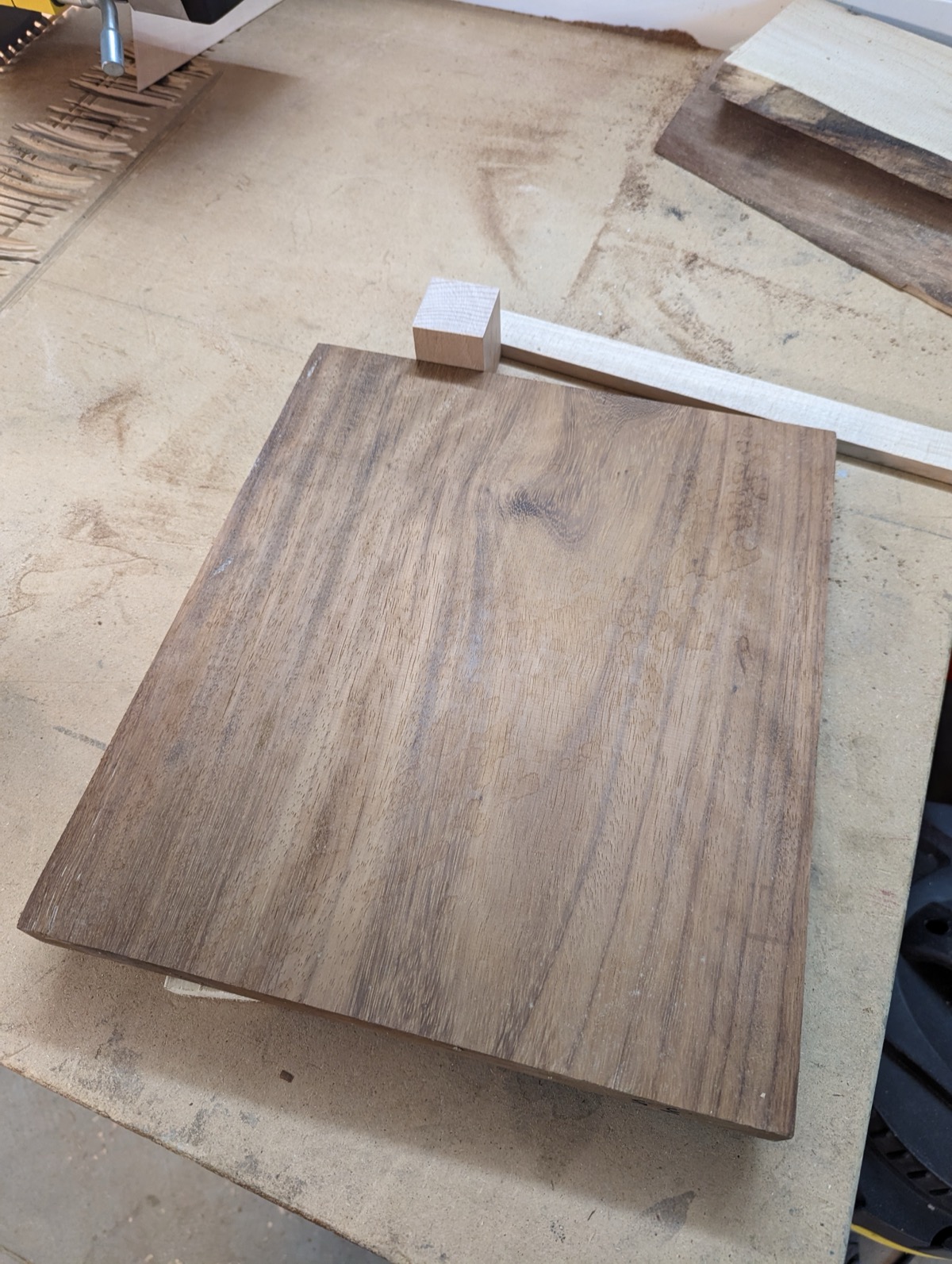 A planed walnut board on the workbench next to offcuts and a length of maple