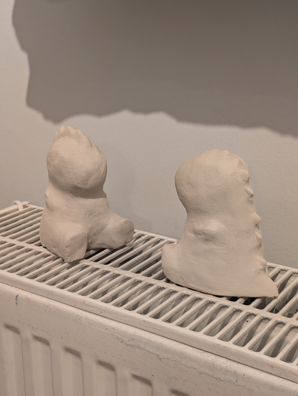 Two unglazed clay dinosaur shapes resting and drying on a counter